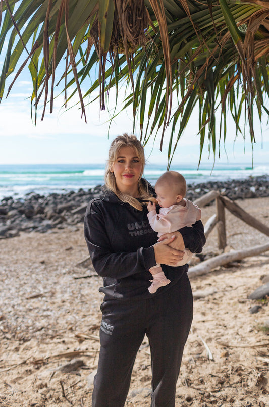 Black breastfeeding-friendly tracksuit with hidden zips, unzipped for easy nursing access, showing a mom comfortably feeding her baby. Super soft fabric, stylish and practical design for nursing mothers.
